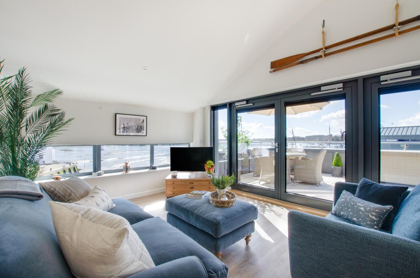 A modern living room with a large window, a flat-screen TV, and a balcony with outdoor furniture.