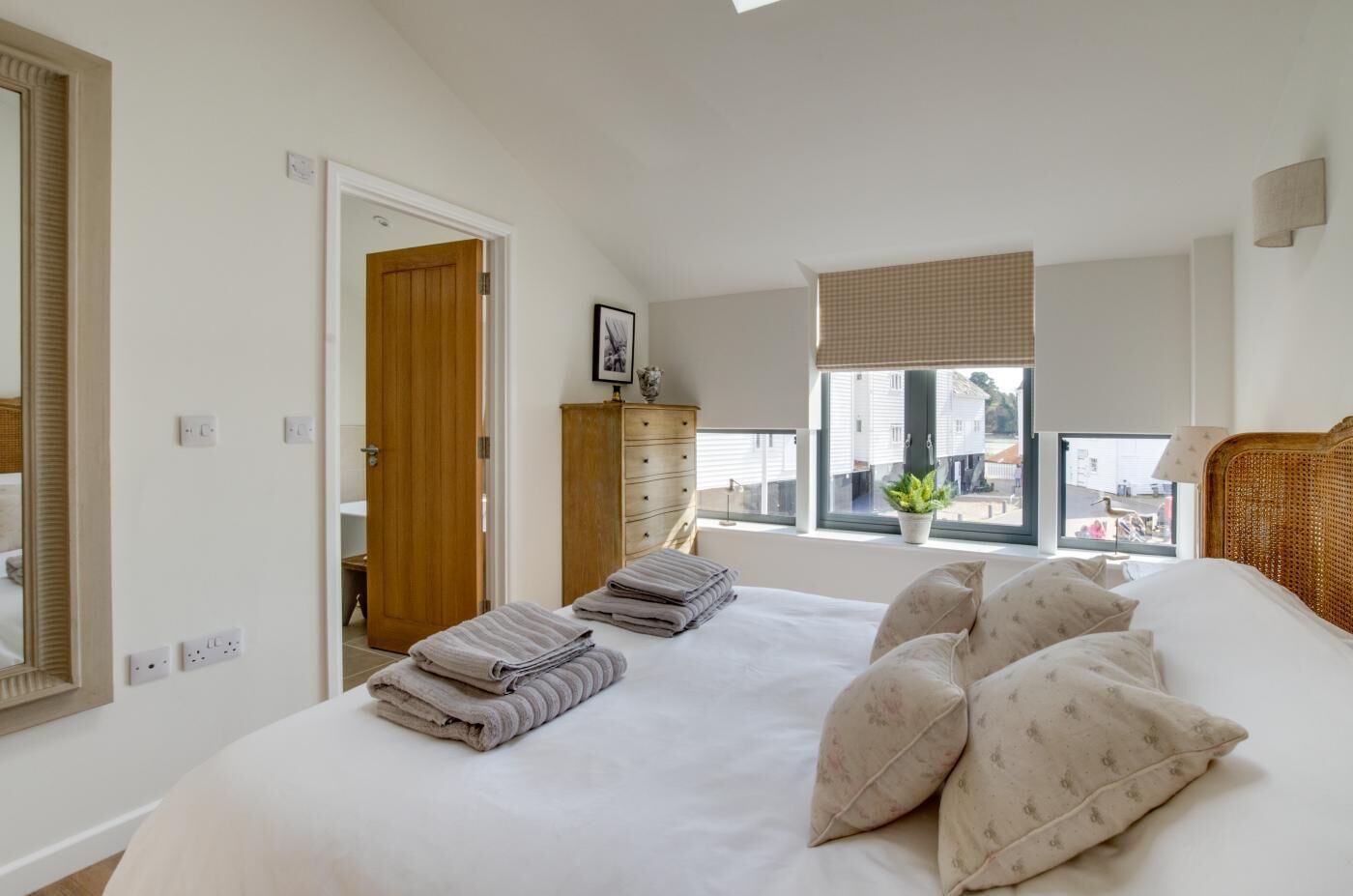 A bedroom with a large bed, a dresser, a window with a view, and a door leading to another room.