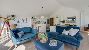 Amplia sala de estar con un sofá azul, una mesa de comedor y una cocina al fondo.