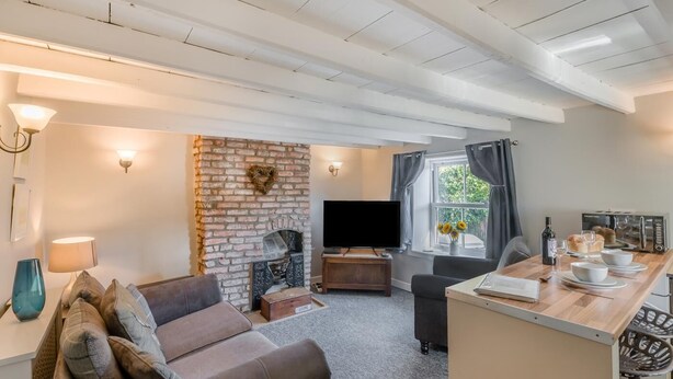 Een gezellige woonkamer met een met baksteen beklede open haard, een flatscreen televisie, een bank en een eethoek met een tafel gedekt voor twee personen.