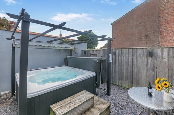 A hot tub under a pergola in a backyard with a wooden fence, a table with a vase of sunflowers, and a bottle of wine. - 1 Bed in Middleton On The Wolds (oc-t32420) (Middleton-on-the-Wolds)