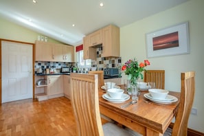 A modern kitchen with wooden cabinets, a dining table set for four, and a vase with flowers.