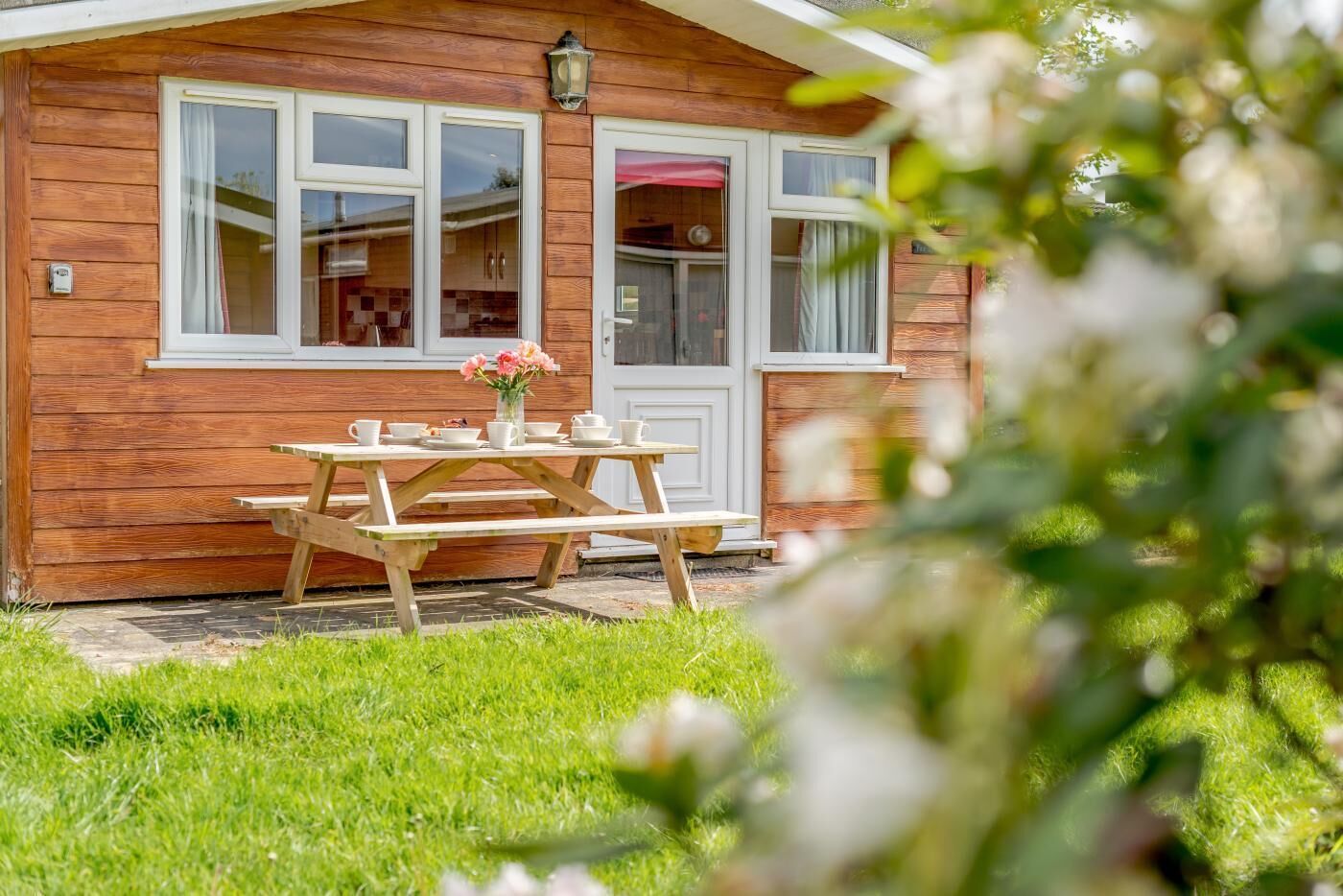 A wooden cabin with a picnic table set up outside, a door with a window, and a small garden area.