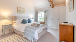 Ein Schlafzimmer mit einem großen Bett, Nachttischen, einem Kleiderschrank und einem Fenster mit Vorhängen.
