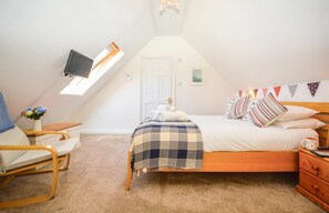 A cozy bedroom with a bed, a chair, a bedside table, and a TV mounted on the sloped ceiling. - 1 Bed in Padstow (oc-p00446) (Padstow)