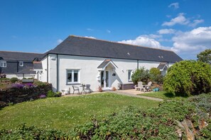 A white house with a grey roof, a front door, and a small patio with outdoor furniture. - 1 Bed in Padstow (oc-p00446) (Padstow)