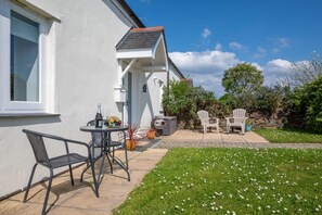 A patio with outdoor furniture, a table with a bottle and fruit, and a stone wall in the background. - 1 Bed in Padstow (oc-p00446) (Padstow)
