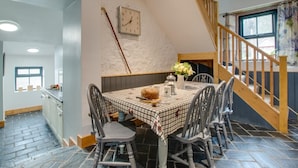 Un comedor con mantel a cuadros, sillas de madera, un reloj en la pared y una escalera que sube a un nivel superior.