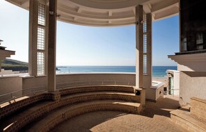 A covered outdoor area with a curved brick bench, a railing, and a view of the sea.
