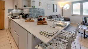 Eine moderne Küche mit Kochinsel, weißen Schränken und einer Essecke inklusive Sofa und Stühlen.