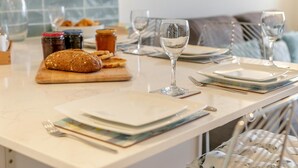 Eine Küchenarbeitsplatte mit Brot, Marmeladengläsern, einem Weinglas und ordentlich drapierten Tellern und Besteck.