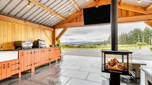 Une cuisine extérieure abritée, dotée d’un poêle à bois, d’une table à manger et offrant une vue sur le paysage.