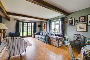 A spacious living room with a wooden floor, a striped armchair, a sofa, and a vintage suitcase. - 3 Bed in Walberswick (oc-spinn) (Walberswick)