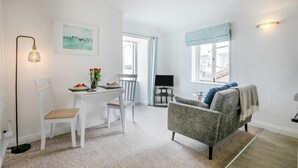 Et værelse med et spisebord, stole, en grå sofa, et fjernsyn og et vindue med gardiner.
