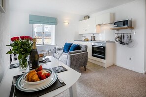 A compact kitchen with white cabinets, a microwave, and a coffee maker. There's a dining area with a table set for two, a vase with flowers, and a plate of strawberries. - 1 Bed in St. Ives (oc-pc466a) (St Ives)