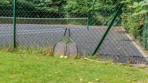 Un terrain de tennis entouré d’une clôture en treillis métallique, avec un poteau vert et une balle de tennis sur le sol.