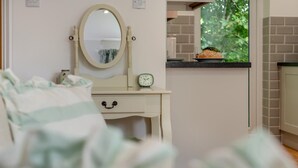 Une chambre à coucher avec un lit, une table de chevet avec une horloge, un miroir et une fenêtre donnant sur un paysage verdoyant.