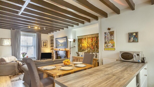 Una sala moderna con una mesa de comedor de madera, un sofá y una chimenea. Hay pinturas en las paredes y un ventanal con cortinas.