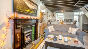 Un salón acogedor con chimenea, un sofá gris y una mesa de centro con libros y bebidas.