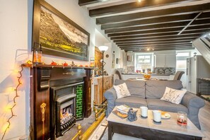 Ein gemütliches Wohnzimmer mit Kamin, einem grauen Sofa und einem Couchtisch mit Büchern und Getränken.