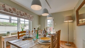 Zona pranzo con tavolo in legno apparecchiato per quattro persone, due lampade a sospensione e una lampada da terra.