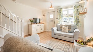 A living room with a sofa, a TV on a cabinet, a staircase, and a window with curtains. - 2 Bed in Padstow (oc-p00407) (Padstow)