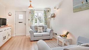 A modern living room with a grey sofa, a television on a wooden cabinet, and a small table with fruit. - 2 Bed in Padstow (oc-p00407) (Padstow)