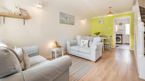 A living room with a sofa, a coffee table, and a dining area with a table and chairs. There is a staircase leading to another level. - 2 Bed in Padstow (oc-p00407) (Padstow)