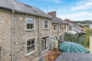 A stone house with multiple windows and a small patio area with a green umbrella. - 3 Bed in Beer (oc-f32429) (Beer)