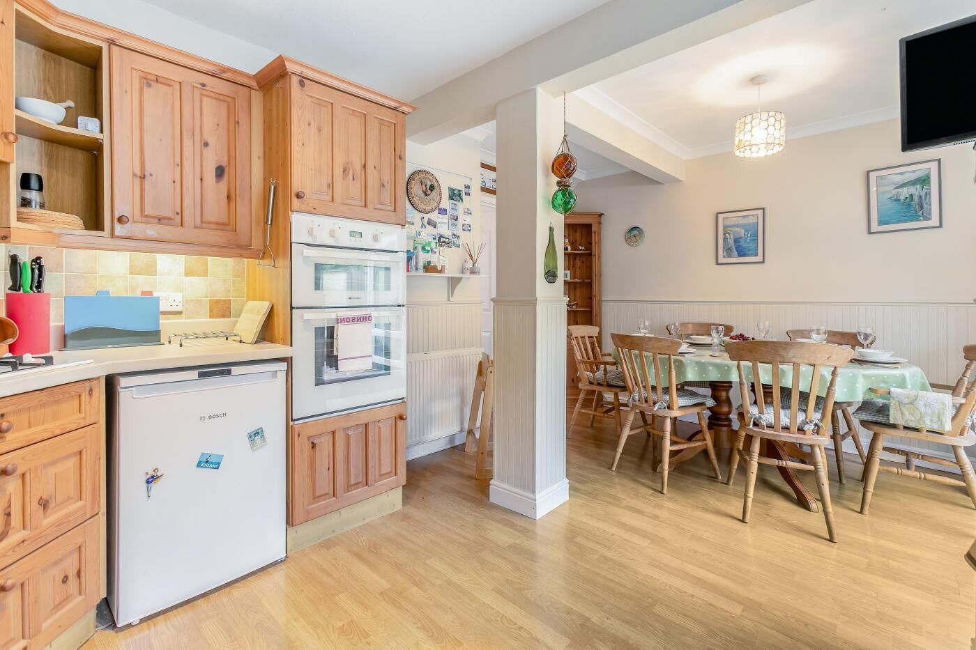 Une cuisine dotée de meubles en bois, d’un réfrigérateur Bosch et d’un coin repas avec des chaises et une table en bois.