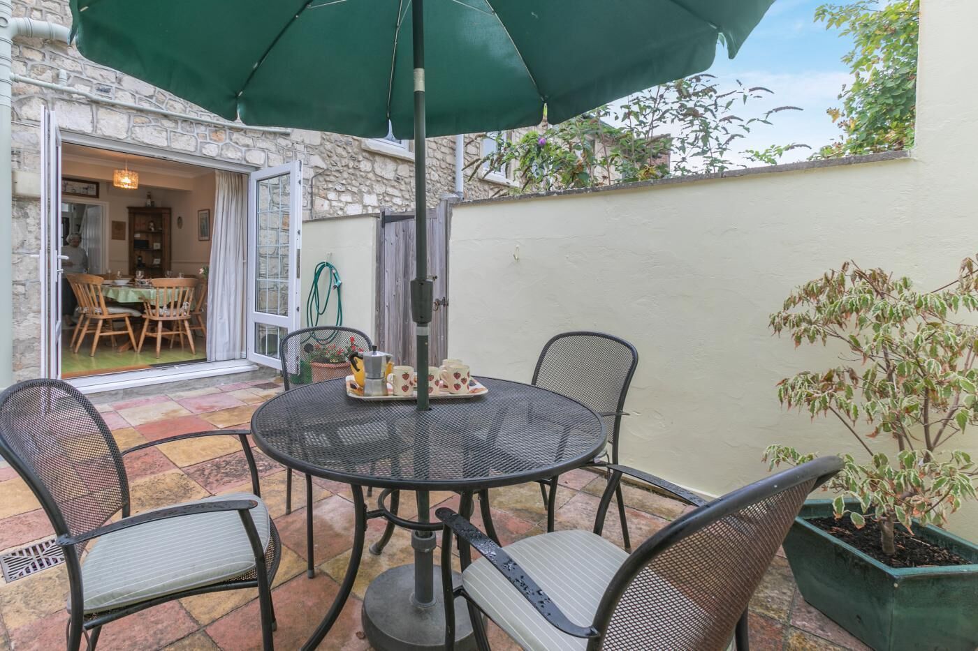 Eine Terrasse mit einem runden Tisch, Stühlen, einem grünen Sonnenschirm und einem Blumentopf.