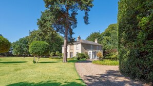 Een groot, twee verdiepingen tellend huis met een grindpad dat leidt naar een verzorgd gazon en een tuin.