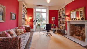Een kamer met een rode wand, een open haard, een boekenkast, een bureau met een lamp, een telescoop en een bank.