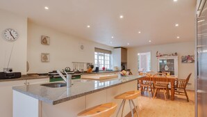Een moderne keuken met een centraal eiland, barstoelen en een eethoek met houten stoelen.