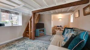 A cozy living room with a wooden staircase, a teal entertainment unit, a beige sofa with teal cushions, and a dining area with a table and chairs. - 1 Bed in Bodham (oc-2141) (Bodham)