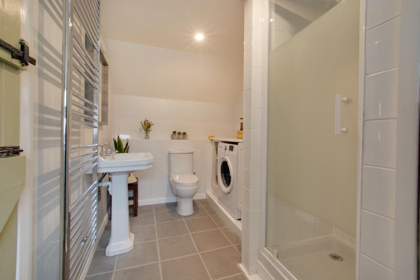A bathroom with a pedestal sink, toilet, washing machine, and a glass-enclosed shower.