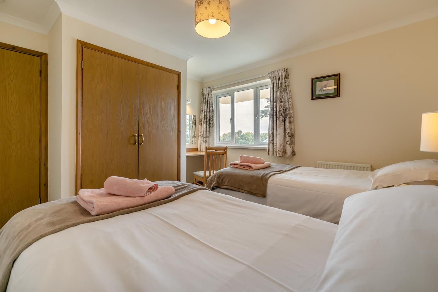 A hotel room with two beds, a desk, a chair, and a window with curtains.