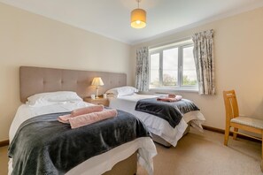 Une chambre d’hôtel avec deux lits, une table de chevet avec une lampe, une fenêtre avec des rideaux et une chaise en bois.