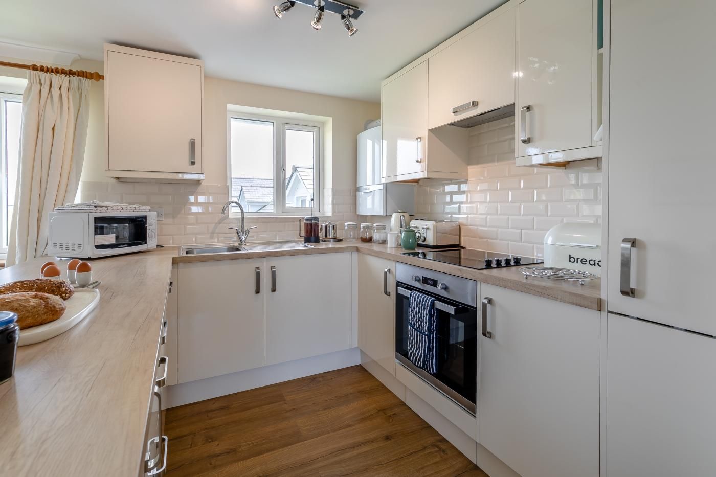 A modern kitchen with white cabinetry, a built-in oven, a microwave, and a window providing natural light.