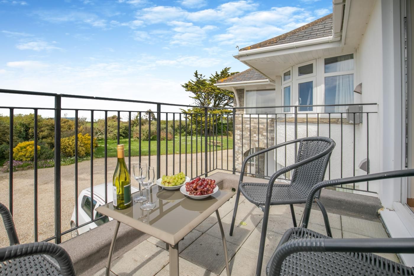 Un balcon avec une table dressée pour deux personnes, une bouteille de vin et un panier de raisins.