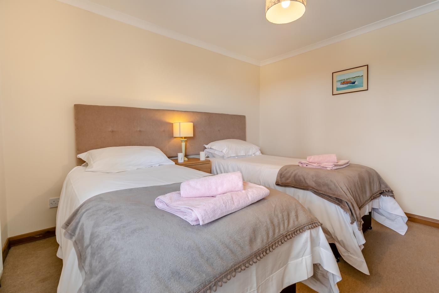 A hotel room with two beds, each with a headboard, a bedside lamp, and neatly folded towels.
