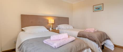 A hotel room with two beds, each with a headboard, a bedside lamp, and neatly folded towels.