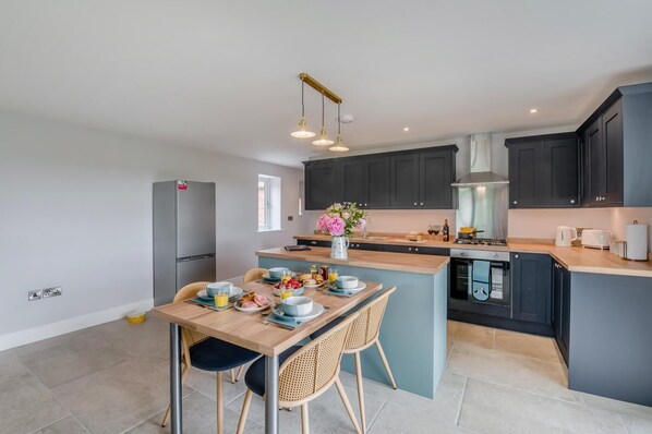A modern kitchen with dark cabinets, a central island, and a dining area with wicker chairs.