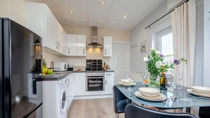 Une cuisine moderne avec des meubles blancs, un réfrigérateur noir et un coin repas avec une table mise pour deux personnes.