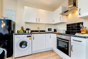 Eine moderne Küche mit weißen Schränken, einer integrierten Waschmaschine, einer Mikrowelle und einem Backofen.