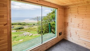 Ein Zimmer mit großem Fenster und Blick auf eine grüne Landschaft und einen fernen Strand.