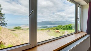 Ein Zimmer mit großem Fenster und Blick auf eine reizvolle Landschaft, einschließlich Bergen und eines Gewässers.
