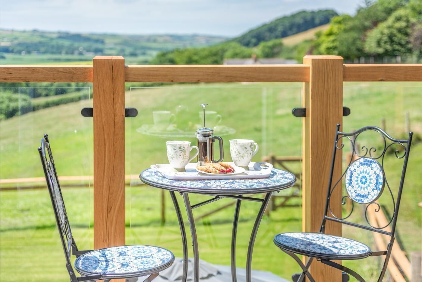 Ein Balkon mit Tisch, der für Tee gedeckt ist, zwei Stühlen und Blick auf sanfte Hügel.