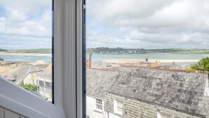 A coastal view from a window overlooking a beach, buildings, and a lighthouse. - 4 Bed in Padstow (oc-p00245) (Padstow)