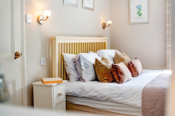 Un lit bien fait, avec une tête de lit en bois, une table de chevet sur laquelle repose un livre et des lampes fixées au mur.